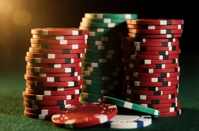 Gestapelte rote und schwarze Casino-Chips auf gr&uuml;nem Filz im warmen Goldlicht - Symbolbild f&uuml;r Slots im V.Vegas Online Casino