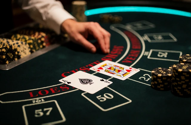 Blackjack-Tisch mit Ass und K&ouml;nig auf gr&uuml;nem Filz neben schwarzen Chips - Black Jack online mit echtem Dealer