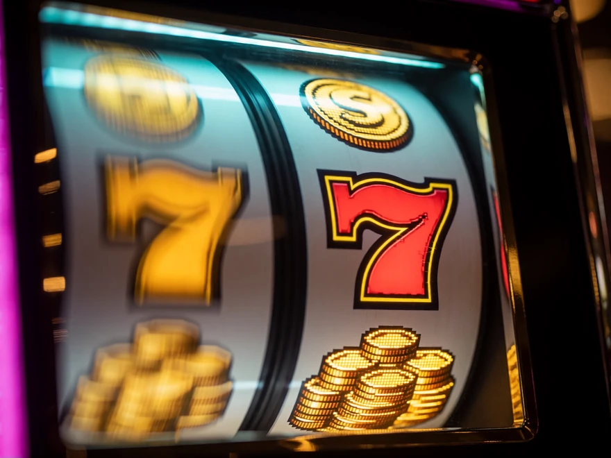 Nahaufnahme einer drehenden Slot-Walze mit leuchtenden M&uuml;nzsymbolen und roter Sieben - Mechanik moderner Online Slots bei V.Vegas